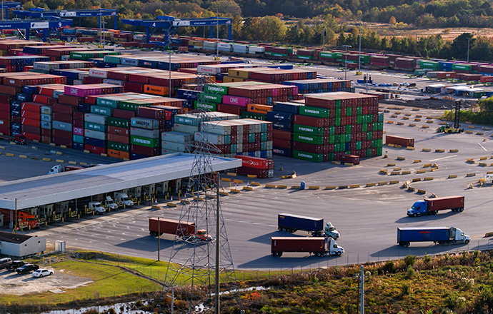 An active shipping yard at the Port of Savannah, Georgia with semi trucks driving around containers.